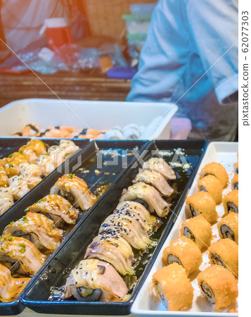 Rows of japanese sushi food. Maki ands rolls with tuna, salmon, shrimp, crab and avocado. Top view of assorted sushi in black plastic container being sale at market. Selective focus. Rows of japanese sushi food. Maki ands rolls with tuna, salmon, shrimp, crab and avocado. Top view of assorted sushi in black plastic container being sale at market. Selective focus. 62077303