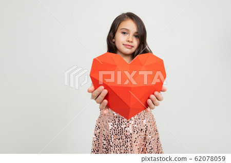 European young girl holding a heart-shaped figure in a studio with light walls European young girl holding a heart-shaped figure in a studio with light walls 62078059