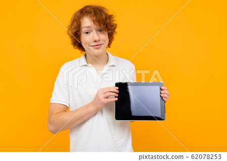 red-haired curly guy in a white T-shirt shows a tablet display with a layout on a yellow background red-haired curly guy in a white T-shirt shows a tablet display with a layout on a yellow background 62078253