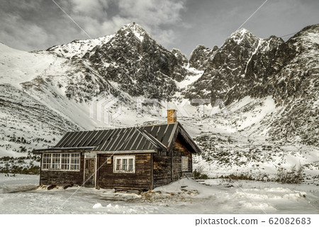 Lonely old wooden cottage and snowy mountains. Lomnicky peak in High Tatras mountains, Slovakia Lonely old wooden cottage and snowy mountains. Lomnicky peak in High Tatras mountains, Slovakia 62082683