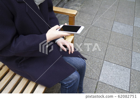 一個女人坐在長凳上操作智能手機 62082751