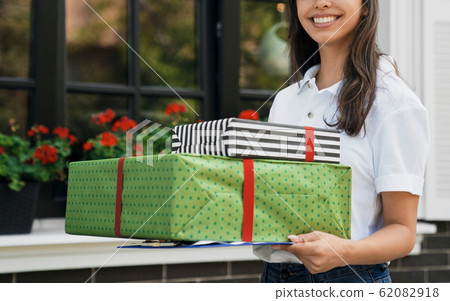 Female courier holding gift boxes and folder. Female courier holding gift boxes and folder. 62082918