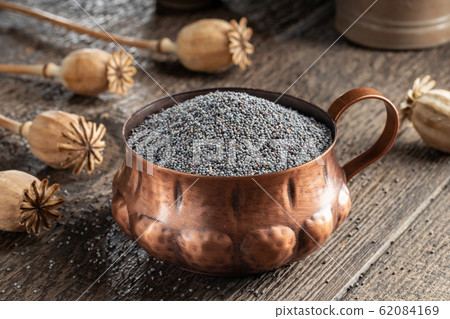 Poppy seeds in a cup with poppy pods in the background 62084169