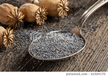 Poppy seeds on a spoon with poppy pods in the background 62084170