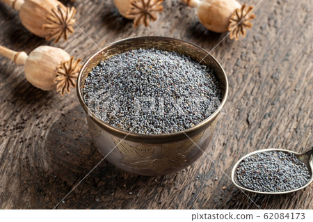 Poppy seeds in a bowl with poppy pods in the background 62084173