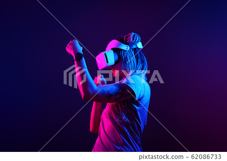 Woman is using virtual reality headset. Neon light studio portrait. 62086733
