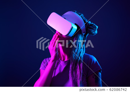 Woman is using virtual reality headset. Neon light studio portrait. 62086742