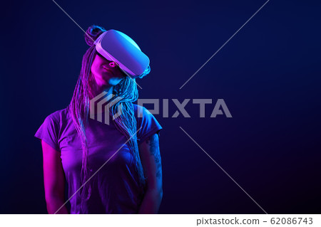 Woman is using virtual reality headset. Neon light studio portrait. 62086743