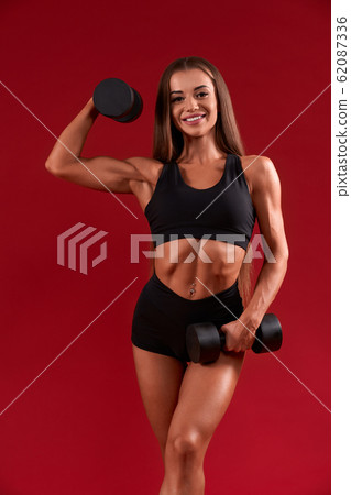 Smiling fitnesswoman training with dumbbells. Smiling fitnesswoman training with dumbbells. 62087336