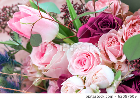 A closeup bouquet of roses and tulips decorated with leaves and twigs of other beautiful plants. 62087609