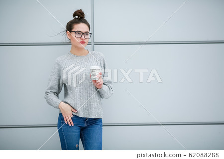 A woman with glasses drinking coffee against a gray wall A woman with glasses drinking coffee against a gray wall 62088288