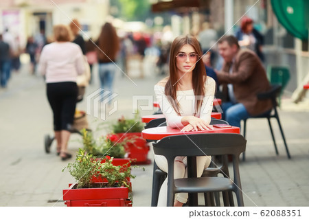 A Young beautiful woman sitting at a table in summer cafe A Young beautiful woman sitting at a table in summer cafe 62088351