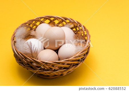 natural ecological eggs and feather in a wicker basket on yellow background with copy space. happy easter 62088552