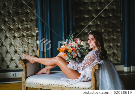 Seductive young bride posing with gorgeous bridal bouquet on a sofa 62088619