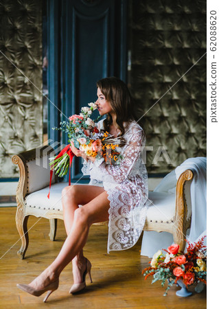 Seductive young bride posing with gorgeous bridal bouquet on a sofa 62088620