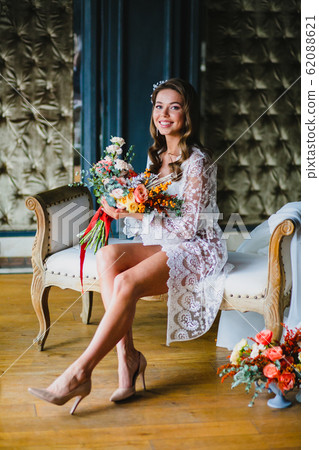 Seductive young bride posing with gorgeous bridal bouquet on a sofa 62088621