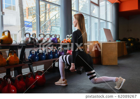 Young sexy woman during fitness workout at gym. Exercises with dumbbells. Squats and lunges. 62089267