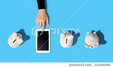 Person using a tablet computer with piggy banks Person using a tablet computer with piggy banks 62089466