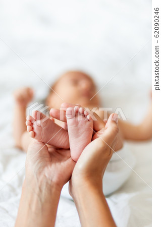 Mother holds newborn baby's bare feet. Tiny feet in woman's hand. Cozy morning at home. 62090246