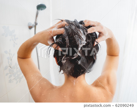 Naked woman with short hair takes a shower. Woman washes her hair with shampoo. White bathroom. Naked woman with short hair takes a shower. Woman washes her hair with shampoo. White bathroom. 62090249