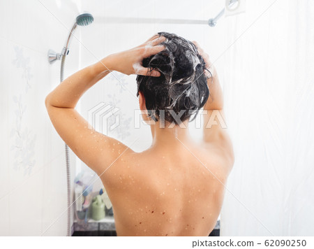 Naked woman with short hair takes a shower. Woman washes her hair with shampoo. White bathroom. Naked woman with short hair takes a shower. Woman washes her hair with shampoo. White bathroom. 62090250