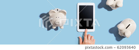 Person using a tablet computer with piggy banks Person using a tablet computer with piggy banks 62093640