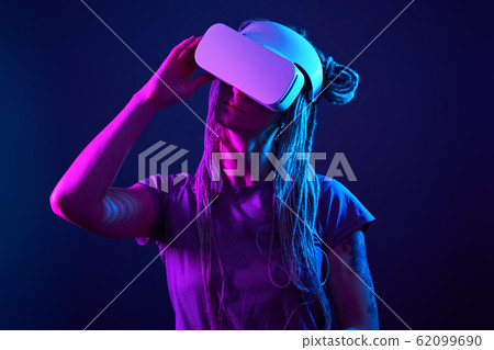 Woman is using virtual reality headset. Neon light studio portrait. 62099690