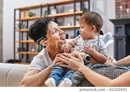 Happy international family concept. Dad, mom, son and little daughter posing for a camera at home, are engaged in home parenting. Home holidays, parenting, concept children and parents. Happy international family concept. Dad, mom, son and little daughter posing for a camera at home, are engaged in home parenting. Home holidays, parenting, concept children and parents. 62102693