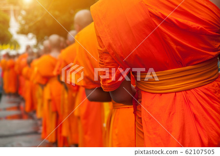 Buddhist philanthropy concept. Buddhist Monks line up in row waiting for Buddhism people to give alms bowl in Thai temple at morning time. Selective focus at front Monk. Light with len flare effect 62107505