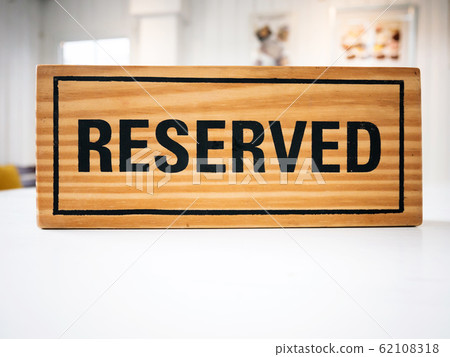 Reservation seat at restaurant for dating on celebrate day concept. Restaurant with reserved wooden sign on white table with cafe decorate places setting and evening light with bokeh for dinner time 62108318