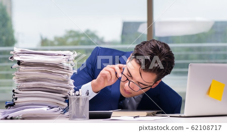 Workaholic businessman overworked with too much work in office Workaholic businessman overworked with too much work in office 62108717