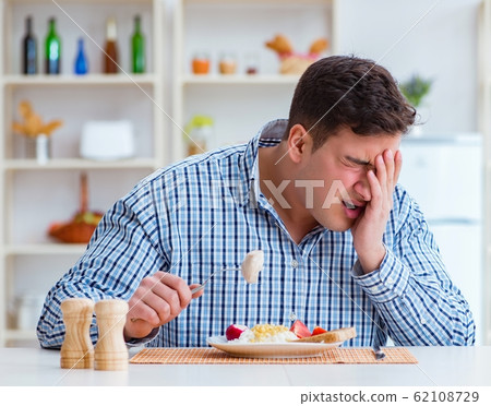 Man eating tasteless food at home for lunch Man eating tasteless food at home for lunch 62108729