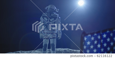 Astronaut standing behind US flag 62116122