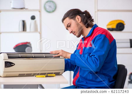 Young male contractor repairing air-conditioner at workshop Young male contractor repairing air-conditioner at workshop 62117243