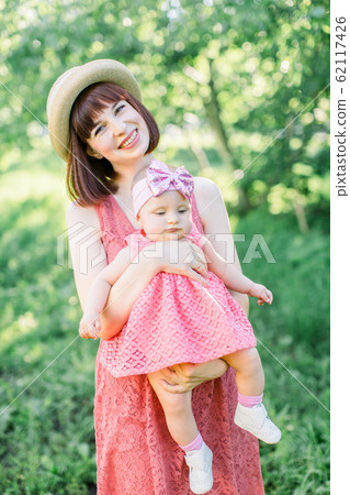 Beautiful Mother with the straw hat And her little daughter outdoors family look in in a pink dress . Young mother with her little baby on the meadow Beautiful Mother with the straw hat And her little daughter outdoors family look in in a pink dress . Young mother with her little baby on the meadow 62117426