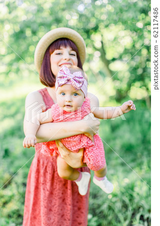 Beautiful Mother with the straw hat And her little daughter outdoors family look in in a pink dress . Outdoor Portrait of happy family. family look. Happy mother having fun with her daughter 62117486