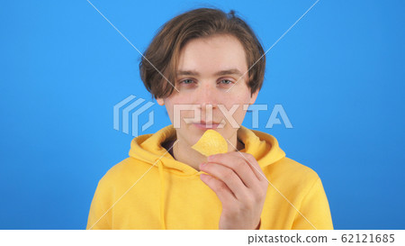 Cheerful guy eating potato chip against blue background 62121685