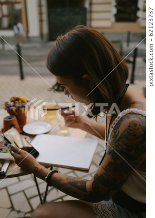 Young woman draws at the sketchbook with a pencil outdoors on the street Young woman draws at the sketchbook with a pencil outdoors on the street 62123737