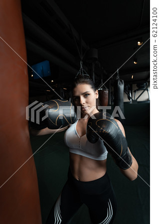 Boxing woman posing with punching bag, on dark background. Strong and independent woman concept Boxing woman posing with punching bag, on dark background. Strong and independent woman concept 62124100