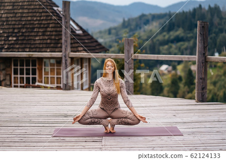 A woman practices yoga at the morning in a terrace on a fresh air. 62124133