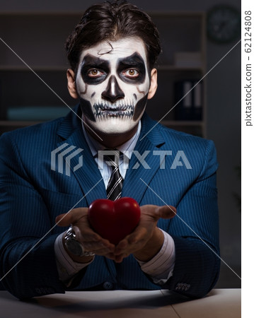 Businessman with scary face mask working late in office 62124808
