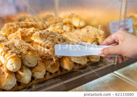 Close up of hand picking pork floss bread with clamp 62133880