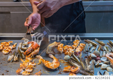 Chef using spatula frying assortment of seafood in restaurant's kitchen 62134101