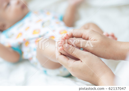 Baby boy foot massage by mom on white blanket 62137047