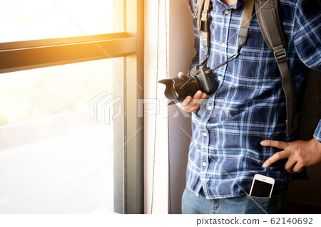 travel and photography concept. photographer with backpack and digital camera standing near window ready to travel for take photo , anonymous face. film effect 62140692