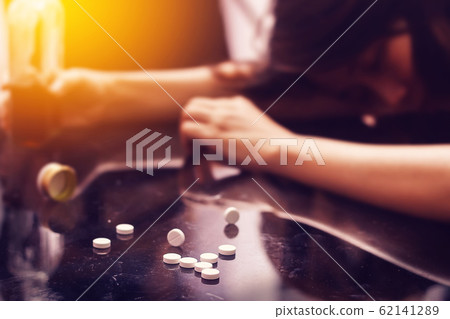 overdose , drug addiction problem concept : Several pill spilled on table Near bottle of alcohol. 62141289