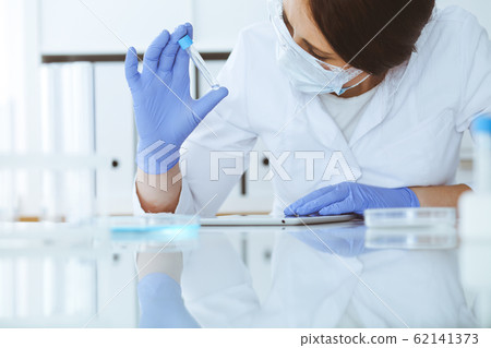 Close-up of professional female scientist in protective eyeglasses making experiment with reagents in laboratory. Medicine and research concept Close-up of professional female scientist in protective eyeglasses making experiment with reagents in laboratory. Medicine and research concept 62141373