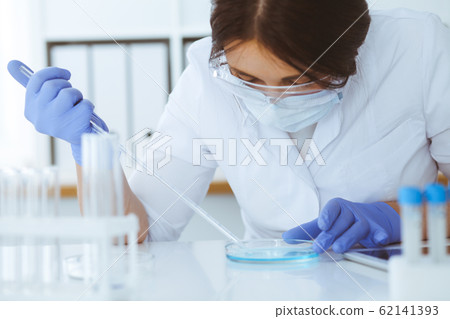 Close-up of professional female scientist in protective eyeglasses making experiment with reagents in laboratory. Medicine and research concept 62141393