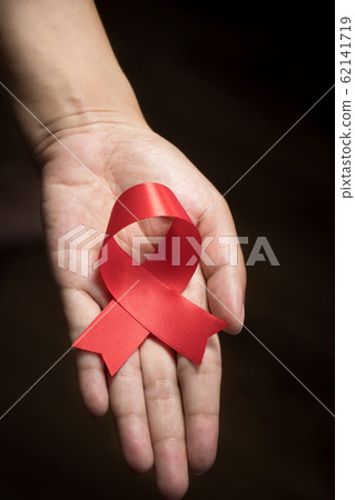 World AIDS Day concept : Red ribbon on human hand isolate on black background. Red ribbon symbolic bow color raising awareness on World AIDS Day , 1 December World AIDS Day concept : Red ribbon on human hand isolate on black background. Red ribbon symbolic bow color raising awareness on World AIDS Day , 1 December 62141719