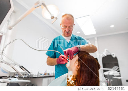 Senior male dentist working with his young patient woman visiting dentist and having dental checkup and treatment at the clinic. Dentistry occupation, treatment concept 62144661
